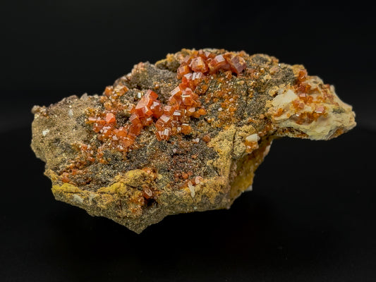 Close-up of Vanadinite crystal specimen from Morocco, featuring red-orange hexagonal formations with a glossy, reflective surface. 